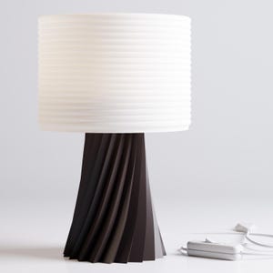 May include: A modern table lamp with a white pleated lampshade and a dark brown, twisted base. The lamp has a white cord and a white switch.