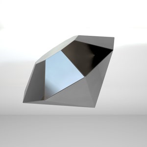Puede incluir: Una escultura geométrica plateada con un diseño facetado. La escultura está hecha de metal y tiene una superficie reflectante.
