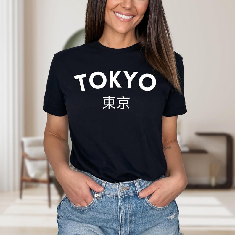 May include: Black t-shirt with the word "TOKYO" in white block letters above Japanese characters. The model is wearing blue denim shorts. The shirt is a crew neck style.