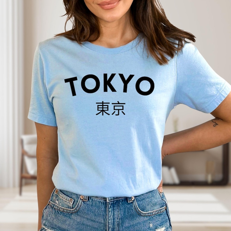 May include: Light blue t-shirt with the word "TOKYO" in bold black letters above Japanese characters. The shirt is made of a soft material and is suitable for casual wear.