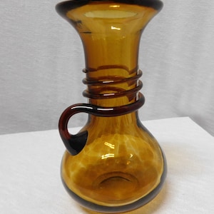 May include: A brown glass vase with a twisted neck and a handle. The vase has a mottled, textured surface.