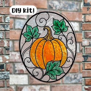 May include: An oval-shaped DIY kit suncatcher featuring a central orange pumpkin with green leaves and black decorative scrollwork outlines. The design is set against a textured, translucent background, and the text DIY kit! is printed in the corner.
