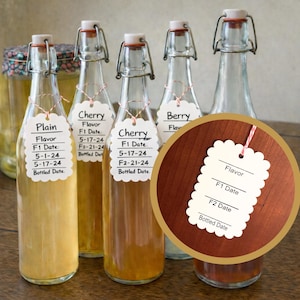 May include: A collection of glass bottles with swing-top lids, each containing a different coloured liquid. The bottles are labelled with flavours such as "Cherry" and "Berry", and dates. The bottles are displayed on a wooden surface.