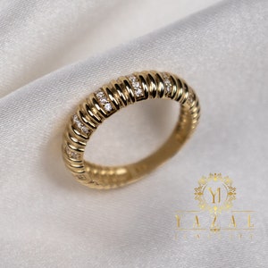 May include: A gold band ring with a textured design and small clear stones set in the band.