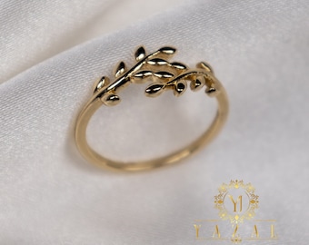 Puede incluir: Un delicado anillo de oro con un diseño de hojas. El anillo está hecho de una fina banda de oro y presenta un delicado diseño de hojas y ramas.