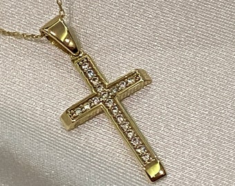 Könnte beinhalten: Eine goldene Kettenkette mit einem kleinen, goldenen Kreuzanhänger, der mit klaren Zirkonia-Steinen besetzt ist.