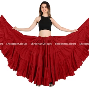 May include: A red, flowing skirt with multiple layers of ruffles. The skirt is being worn by a person with a black tank top.