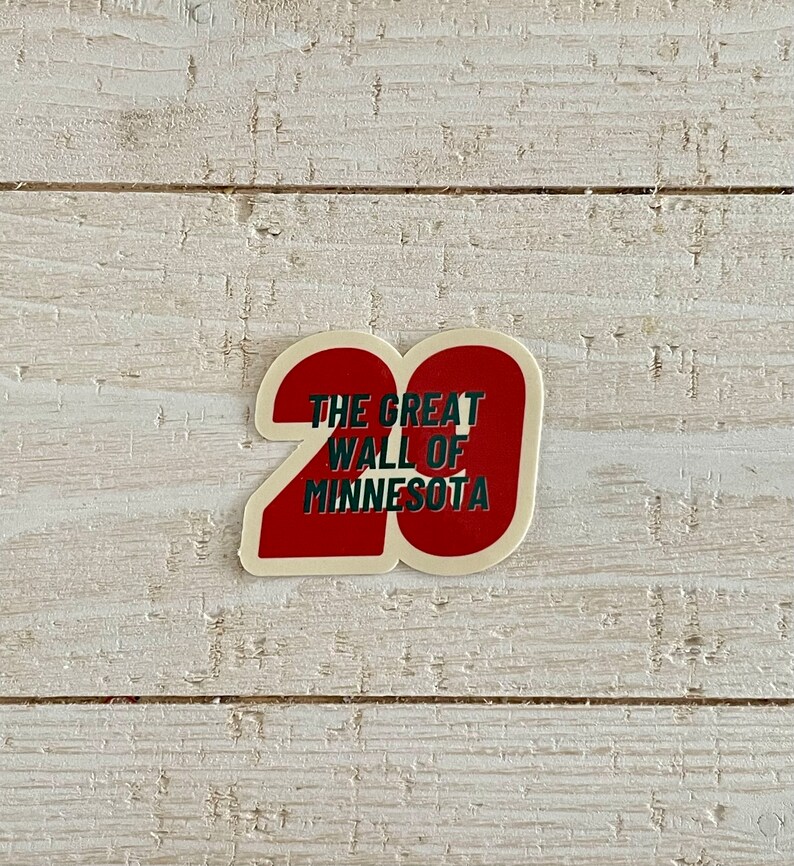 May include: A sticker with a red number 20 shape and the text "THE GREAT WALL OF MINNESOTA" in white and green. The sticker is on a white wooden surface.