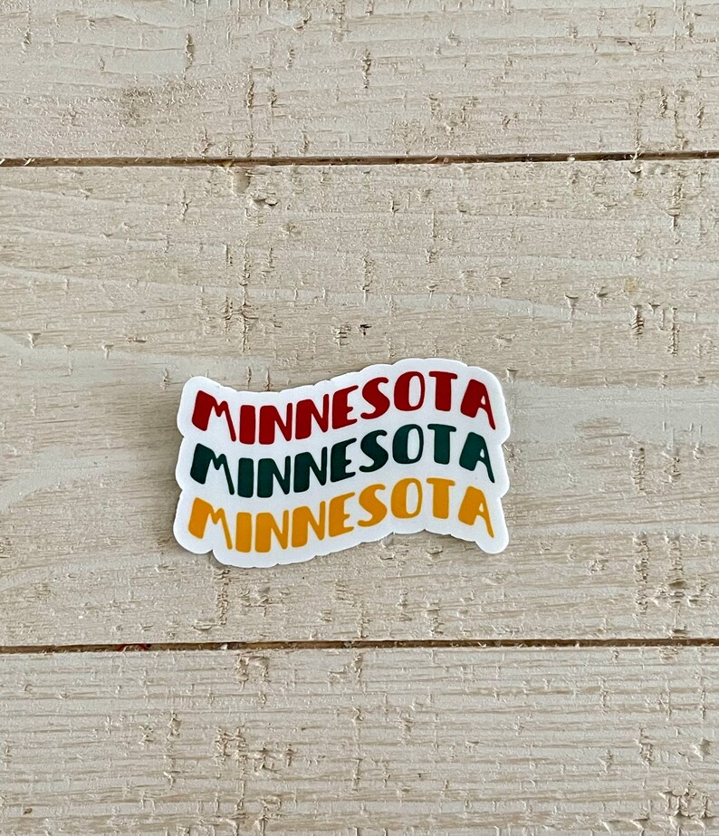 May include: A white sticker with the word "MINNESOTA" stacked three times in red, green, and yellow. The sticker is on a light wood-grain surface.
