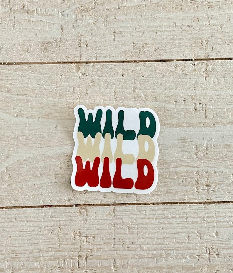 May include: A sticker with the word "WILD" stacked three times in different colors: dark green, tan, and red. The sticker is on a light wood surface.