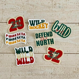 May include: A collection of colorful stickers with text related to Minnesota and hockey. The stickers feature phrases like "Wild Hockey," "Defend the North," and "The Great Wall of Minnesota." The color palette includes green, red, yellow, and white.