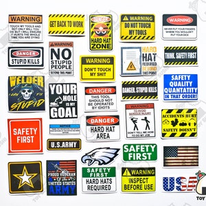 May include: A collection of 25 colorful stickers with various safety slogans and warnings. The stickers feature a variety of designs, including skulls, stars, eagles, and flags. Some of the slogans include "Danger Stupid Kills", "Safety First", "Think Safety First", and "Hard Hat Required".