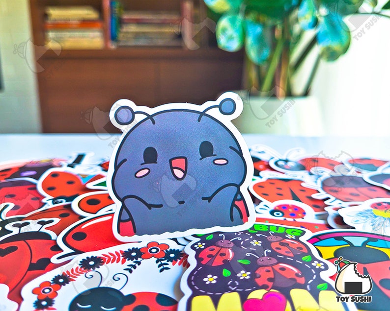 May include: A collection of colorful ladybug stickers with a cartoon ladybug sticker in the center. The cartoon ladybug is blue and gray with a big smile and two antennas. The stickers are perfect for decorating journals, laptops, water bottles, and other items.