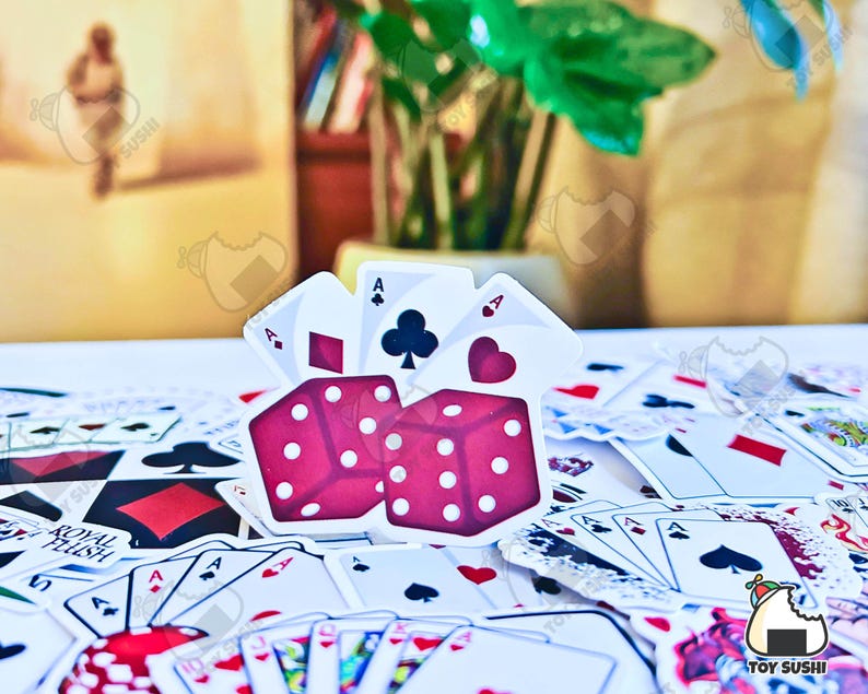 May include: A set of red dice with white dots, surrounded by playing cards. The dice are in the shape of a cube and have a heart symbol on one side. The cards are all face down and are arranged in a random pattern.