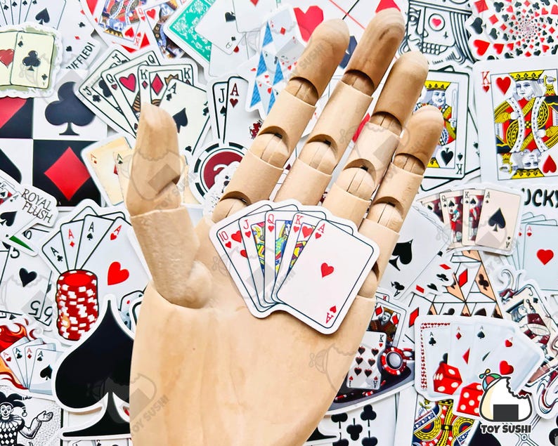 May include: A wooden hand holding a set of playing cards. The cards are all face up and show the numbers 10, Jack, Queen, King, and Ace. The cards are all hearts. The hand is surrounded by a variety of playing cards, including a royal flush, a joker, and a few other cards.