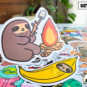 May include: A set of stickers featuring cute cartoon sloths. The stickers include a sloth roasting marshmallows over a campfire, a sloth eating a banana, and a sloth holding a book. The stickers are perfect for adding a touch of whimsy to your laptop, water bottle, or planner.
