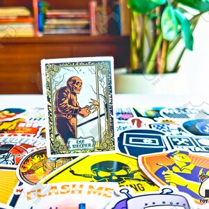May include: A sticker featuring a skeletal figure welding, with the text "The Welder" in a decorative frame. The sticker is surrounded by other colorful stickers with various designs and text, including welding-related imagery.