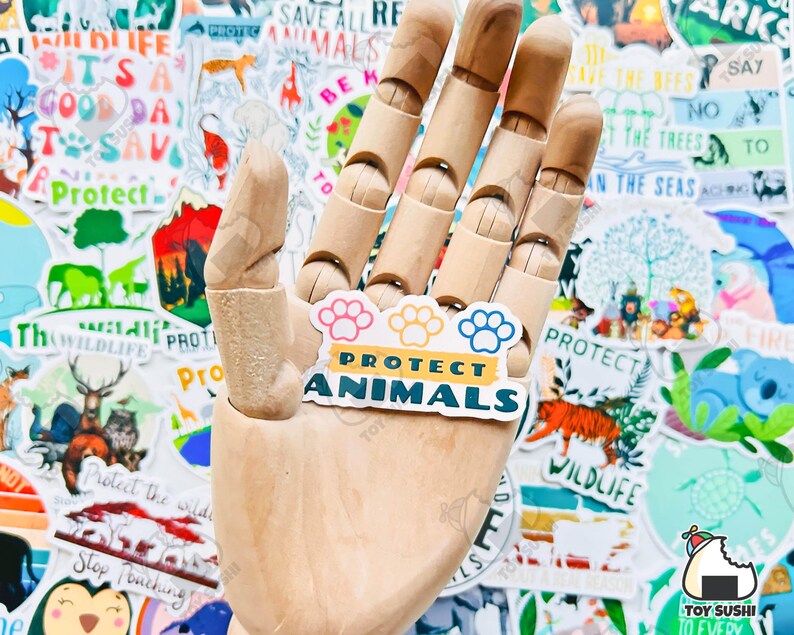 May include: A sticker with a paw print design and the text "Protect Animals" in yellow and blue letters on a white background. The sticker is held by a wooden hand.