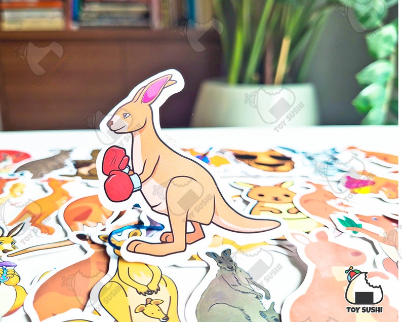 May include: A sticker of a cartoon kangaroo wearing boxing gloves. The kangaroo is brown and has a white belly. The sticker is on a white background with other stickers of animals.