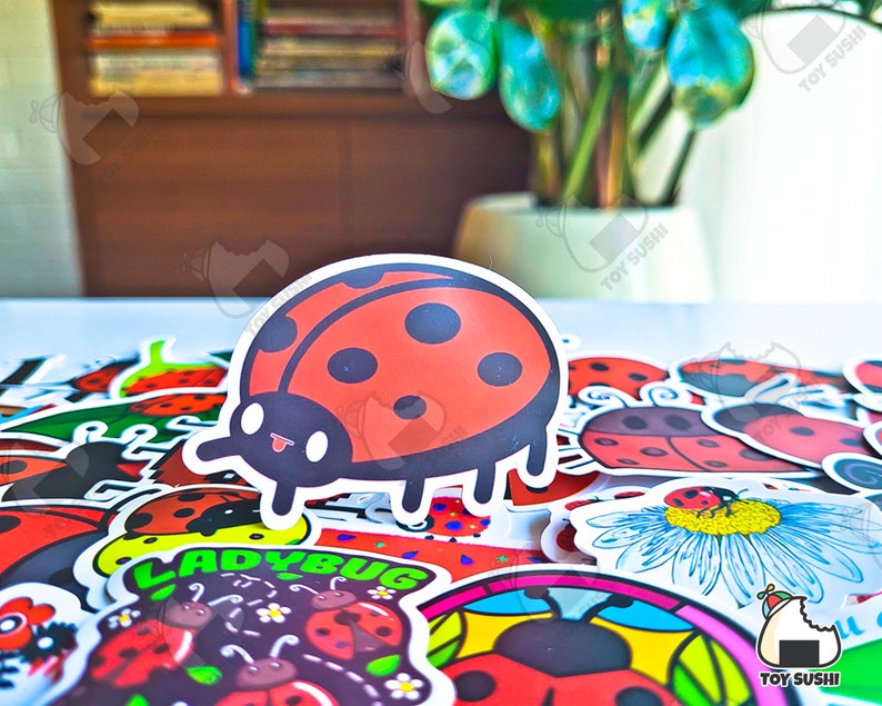 May include: A collection of colorful ladybug stickers with a cartoon ladybug sticker in the center. The stickers feature various designs, including a ladybug on a flower, a ladybug with the word "ladybug" written below it, and a ladybug with black dots on its red shell.