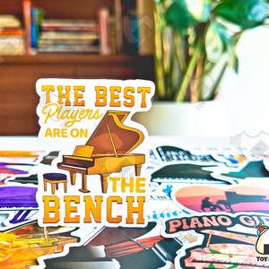 May include: A sticker with a yellow and brown piano and the text "The Best Players Are On The Bench".