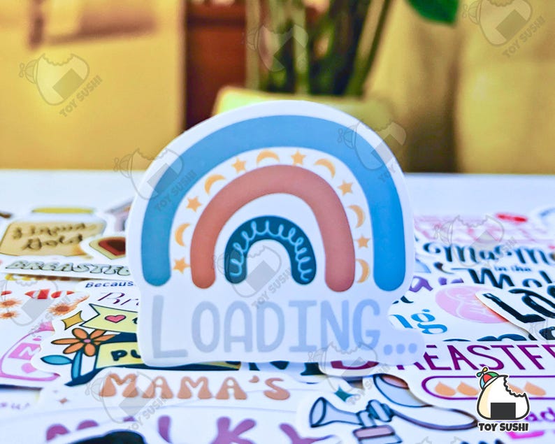 May include: A sticker featuring a rainbow design with the text "LOADING..." in white. The rainbow is made up of blue, pink, and orange stripes with white stars and crescent moons.