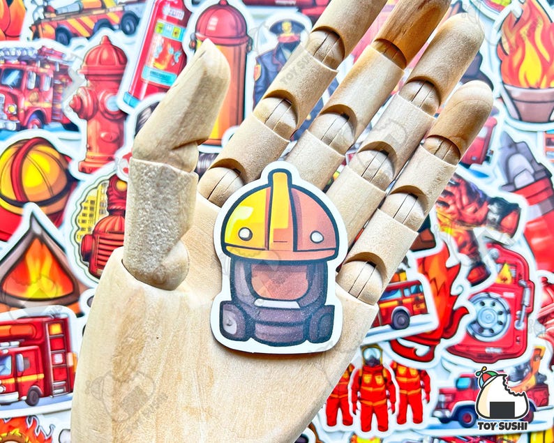 May include: A cartoon firefighter sticker with a yellow helmet and a red and black fire suit. The sticker is on a wooden hand surrounded by other fire-themed stickers.
