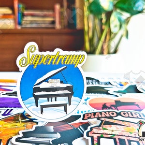 May include: A sticker with a blue background and a white grand piano with the text "Supertramp" in yellow letters.