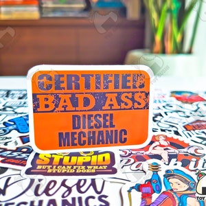 May include: A collection of colorful stickers with various designs, including a sticker that reads "Certified Bad Ass Diesel Mechanic".