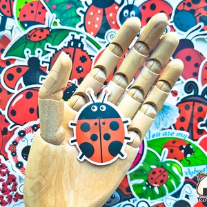 May include: A wooden hand holding a red and black ladybug sticker. The sticker has white spots and black eyes. The hand is surrounded by a variety of ladybug stickers in different designs and colors.