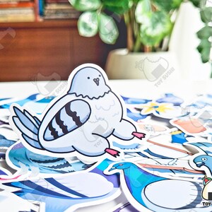 May include: A collection of colourful cartoon bird stickers, including a blue pigeon with black stripes, a blue bird with a long neck, and a white bird with a black beak. The stickers are on a white surface.