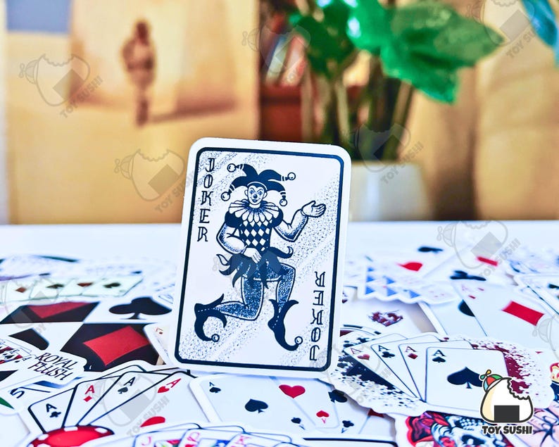 May include: A playing card with a joker design. The joker is depicted as a jester with a black and white harlequin costume. The card is white with black text that reads "JOKER" on the left side and "JOKER" vertically on the right side.