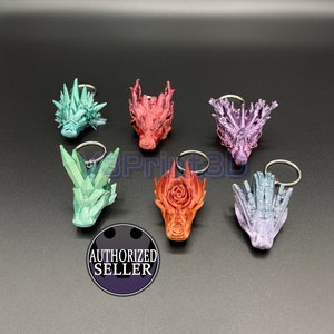 Puede incluir: Seis llaveros de cabeza de dragón de diferentes colores. Los llaveros están hechos de un material plástico impreso en 3D. Los colores son rojo, verde, morado, azul y dos tonos de rosa.