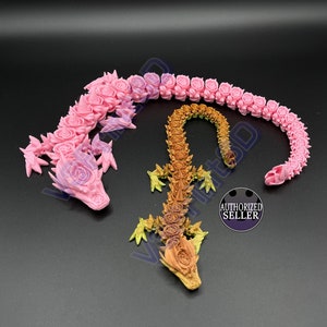 Puede incluir: Dos figuritas de dragón impresas en 3D, una rosa y otra marrón, hechas de rosas. El dragón rosa está enroscado en un círculo, mientras que el dragón marrón está de pie. Ambos dragones tienen escamas y alas detalladas.