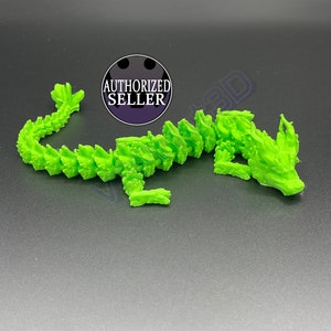 Puede incluir: Una figurita de dragón impresa en 3D de color verde brillante con textura escamosa. El dragón está enroscado en una posición de descanso con la cabeza apoyada en sus patas delanteras.