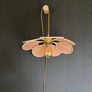 Puede incluir: Una lámpara con forma de flor con una bombilla colgando de ella. La flor está hecha de madera y tiene un color marrón claro. La bombilla es una bombilla de estilo vintage con un vidrio transparente y un filamento.