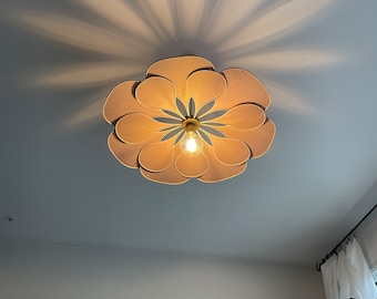 May include: A beige flower-shaped ceiling light fixture with a single light bulb in the center. The light fixture casts a shadow on the ceiling.