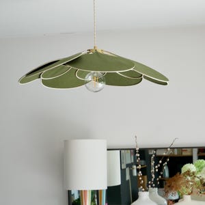 Peut inclure: Un luminaire suspendu en tissu vert en forme de fleur à plusieurs couches. Le luminaire est suspendu à un plafond blanc et possède une seule ampoule.