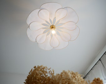 May include: White ceiling light fixture shaped like a flower with multiple petals. The light fixture is made of a translucent material and has a gold-coloured centre.