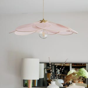 May include: A pink, layered, flower-shaped pendant light fixture hangs from the ceiling. The light fixture is made of thin, translucent fabric and has a gold-coloured metal frame. The light fixture is illuminated by a single light bulb.