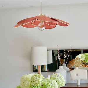 Op de afbeelding: Een roze en witte bloemvormige hanglamp hangt aan het plafond. De lamp is gemaakt van meerdere overlappende bloemblaadjes. De lamp wordt verlicht door een enkele gloeilamp.
