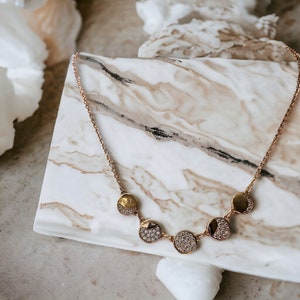 May include: A gold necklace with a delicate chain and five round pendants. Each pendant is encrusted with small, clear stones and has a smooth, gold surface.