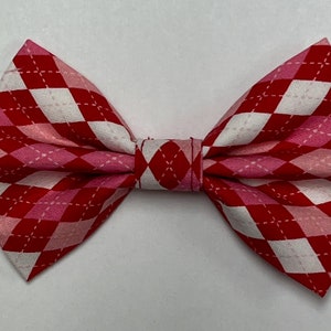 May include: A red and pink bow tie with a white diamond pattern. The bow tie is made of fabric and has a stitched edge.