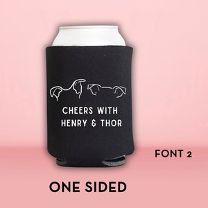 Peut inclure: Glaci&egrave;re en n&eacute;opr&egrave;ne noire avec du texte blanc qui dit "Cheers with Henry & Thor" et un dessin au trait de trois chiens. La glaci&egrave;re est unilat&eacute;rale et porte le texte "FONT 2" imprim&eacute; en dessous.