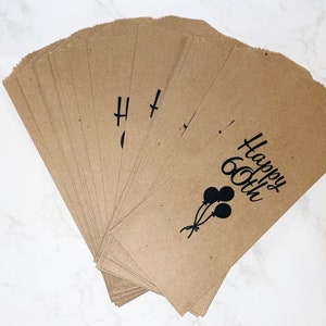 May include: A stack of brown paper bags with black text that reads "Happy 60th" and a black silhouette of balloons.