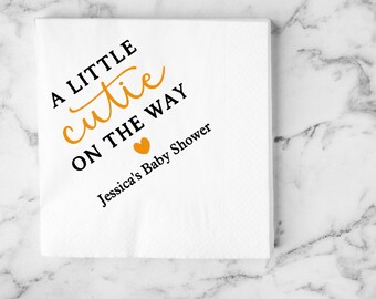 Peut inclure: Serviette en papier blanche avec du texte noir qui dit "A little cutie on the way Jessica's Baby Shower" avec un cœur doré.