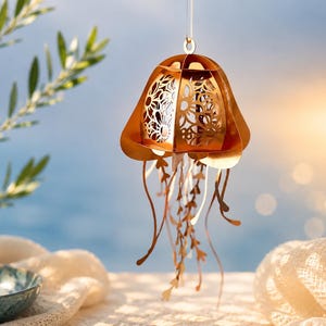 May include: A hanging ornament shaped like a jellyfish, constructed from metallic copper-colored material with intricate laser-cut floral patterns on the bell and multiple thin, dangling ribbon-like tentacles extending from the base.
