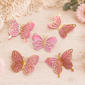 Pode incluir: Cinco recortes decorativos de borboletas com um design em camadas, apresentando asas de papel rosa s&oacute;lido por baixo e sobreposi&ccedil;&otilde;es de filigrana met&aacute;lica dourada. Cada borboleta exibe uma forma de asa e um padr&atilde;o &uacute;nicos e distintos.