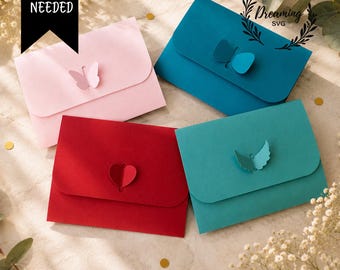 May include: Four rectangular paper envelopes in light pink, dark blue, red, and teal. Each envelope features a die-cut butterfly or heart shape on the flap. Text on the image reads NO GLUE NEEDED and Dreaming SVG. SVG | DXF | EPS | PNG | PDF.