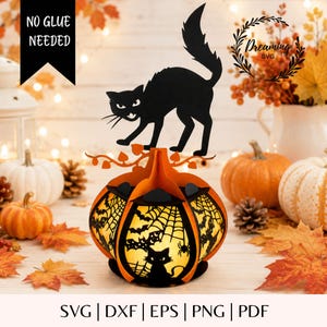 May include: A 3D paper craft pumpkin lantern featuring a black cat silhouette on top and intricate cutouts of bats, spiderwebs, and cats on the orange panels. The design includes the text NO GLUE NEEDED and Dreaming SVG in the corners.